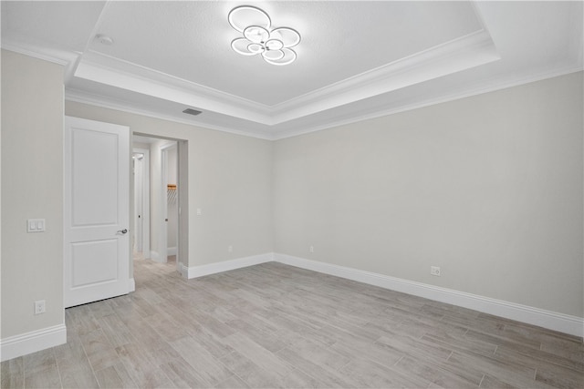 spare room featuring light wood-type flooring, a raised ceiling, a textured ceiling, and crown molding