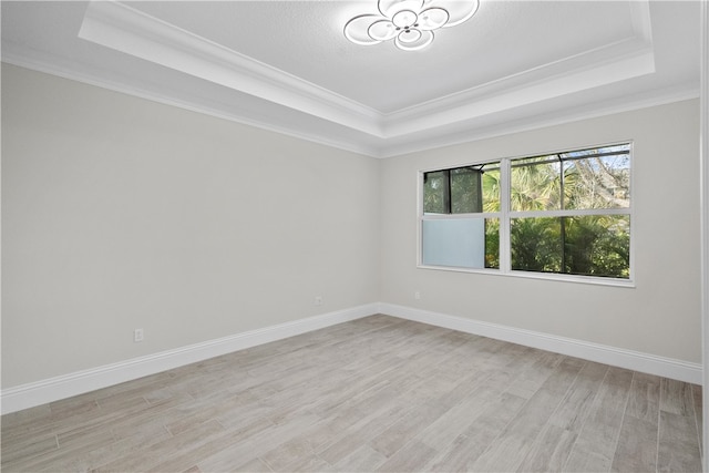 empty room with ornamental molding, light hardwood / wood-style flooring, and a raised ceiling