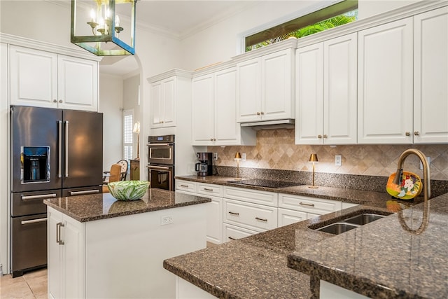 kitchen with white cabinetry, appliances with stainless steel finishes, dark stone counters, and decorative light fixtures