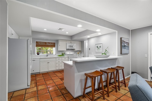 kitchen featuring sink, kitchen peninsula, white appliances, a breakfast bar, and white cabinets