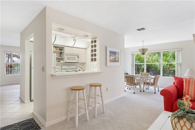 kitchen featuring a textured ceiling, white cabinets, light colored carpet, and white appliances