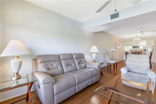 living room featuring ceiling fan with notable chandelier, visible vents, baseboards, and wood finished floors