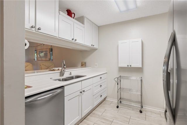 kitchen featuring light countertops, appliances with stainless steel finishes, white cabinets, a sink, and baseboards