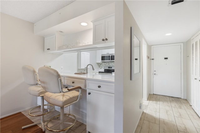 kitchen with white cabinetry, appliances with stainless steel finishes, tasteful backsplash, and light hardwood / wood-style flooring