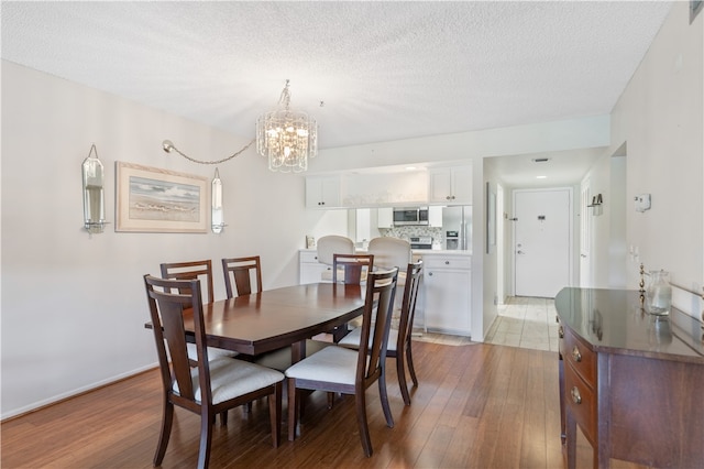 dining space with an inviting chandelier, a textured ceiling, baseboards, and wood finished floors