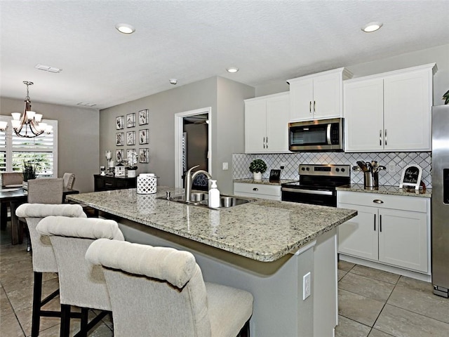 kitchen featuring white cabinetry, sink, hanging light fixtures, an island with sink, and appliances with stainless steel finishes