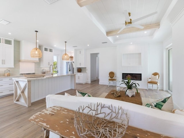 kitchen with light wood finished floors, a large fireplace, beamed ceiling, freestanding refrigerator, and light countertops