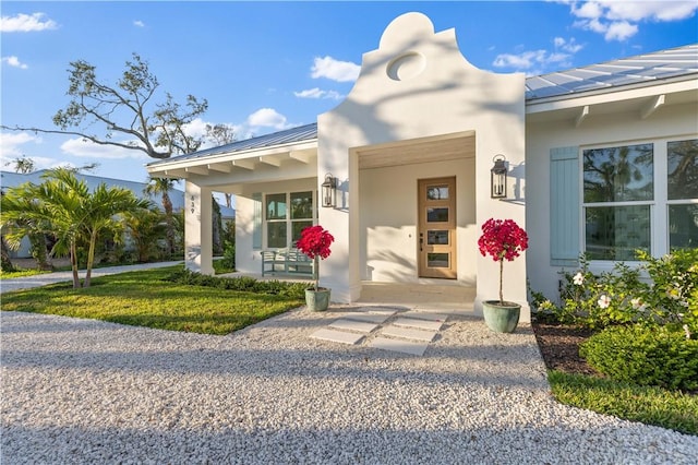 property entrance with a standing seam roof, covered porch, metal roof, and stucco siding