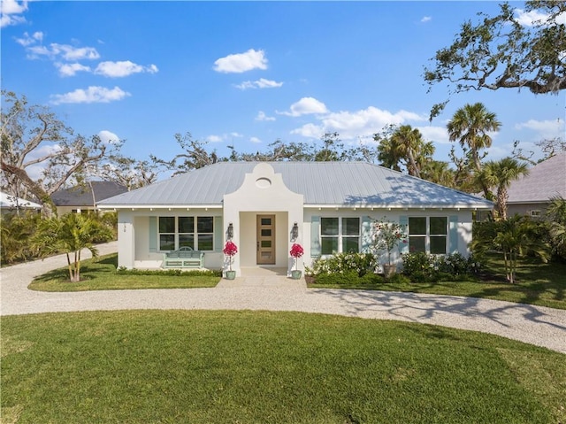 ranch-style house with gravel driveway, metal roof, a front lawn, and stucco siding