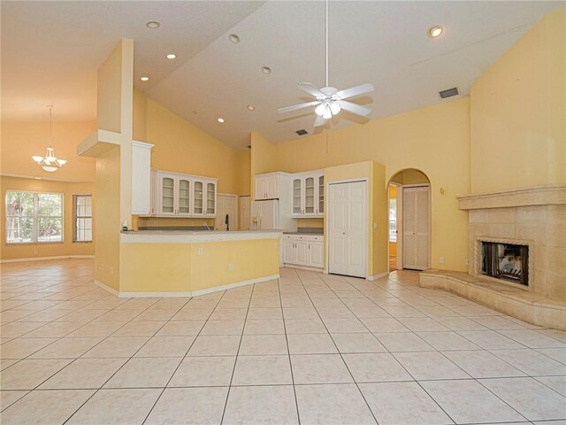 kitchen featuring a tile fireplace, white fridge with ice dispenser, high vaulted ceiling, white cabinets, and ceiling fan with notable chandelier