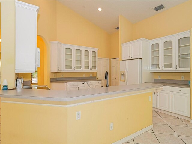 kitchen with high vaulted ceiling, white cabinets, light tile patterned floors, white fridge with ice dispenser, and stainless steel range