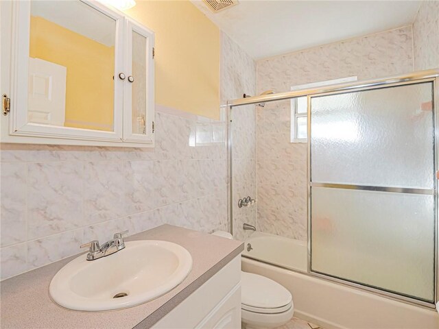 full bathroom featuring vanity, toilet, shower / bath combination with glass door, and tile walls