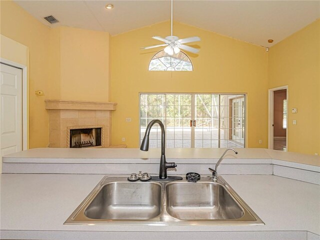 kitchen with a tile fireplace, ceiling fan, sink, and high vaulted ceiling