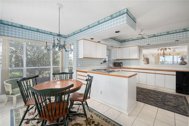 kitchen with stainless steel gas cooktop, hanging light fixtures, light tile patterned floors, white cabinets, and backsplash