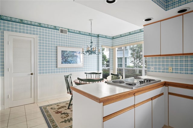 kitchen featuring light tile patterned floors, stainless steel cooktop, white cabinetry, hanging light fixtures, and kitchen peninsula