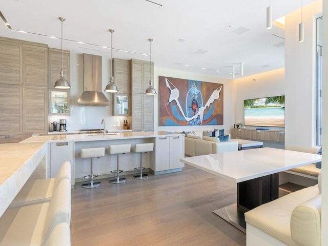 kitchen featuring a breakfast bar, wall chimney range hood, pendant lighting, white cabinets, and hardwood / wood-style floors