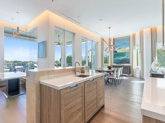 kitchen with light wood-type flooring, sink, hanging light fixtures, and an island with sink