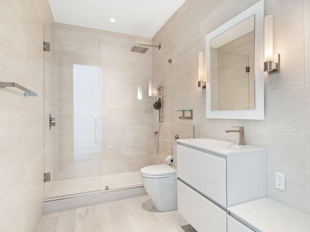 bathroom with vanity, a shower with door, toilet, and tile walls