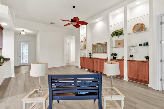 living room featuring light wood-type flooring, built in shelves, and ceiling fan