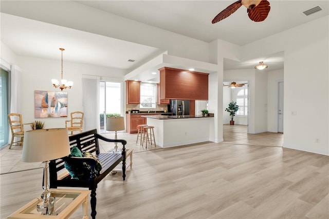 kitchen featuring kitchen peninsula, stainless steel fridge, plenty of natural light, ceiling fan with notable chandelier, and light hardwood / wood-style floors