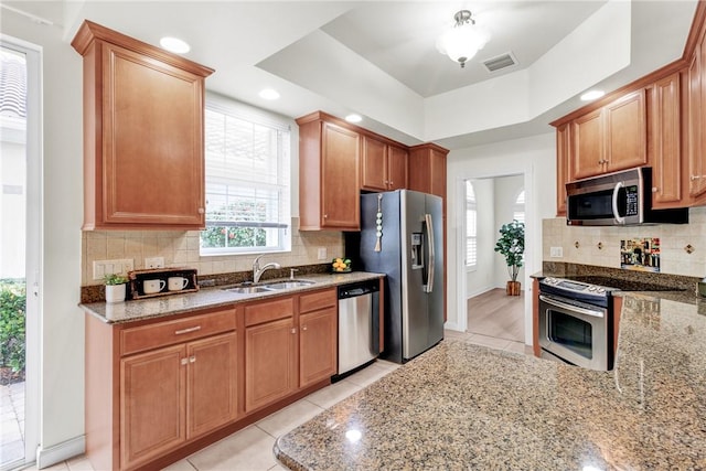 kitchen with stainless steel appliances, sink, a raised ceiling, light stone counters, and light tile patterned floors