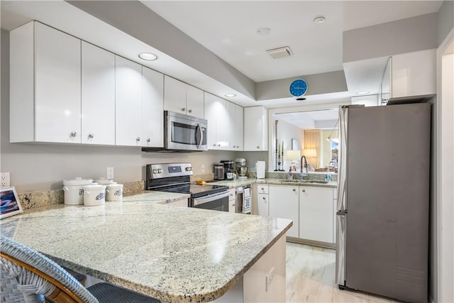 kitchen featuring light stone counters, stainless steel appliances, white cabinets, a sink, and a peninsula