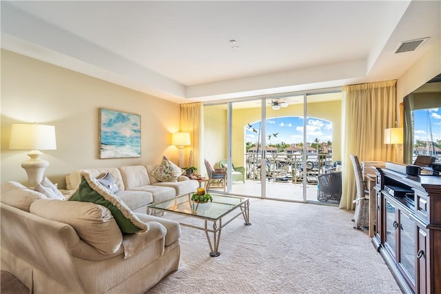 carpeted living room featuring visible vents, a raised ceiling, and a wealth of natural light