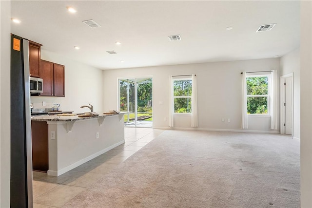 kitchen featuring a breakfast bar, light stone counters, light colored carpet, and appliances with stainless steel finishes