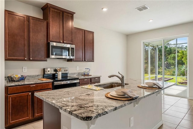 kitchen with light stone countertops, a kitchen island with sink, sink, and stainless steel appliances