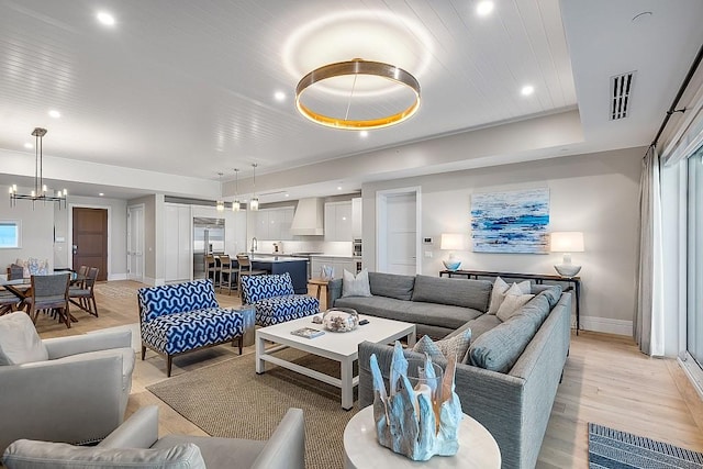 living room with wood ceiling, a chandelier, a raised ceiling, and light wood-type flooring