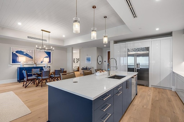 kitchen featuring appliances with stainless steel finishes, sink, hanging light fixtures, a raised ceiling, and a center island with sink