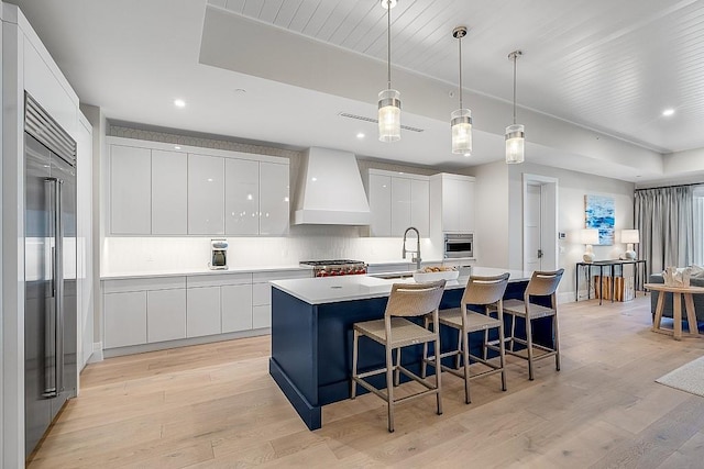 kitchen with premium range hood, decorative light fixtures, white cabinetry, light hardwood / wood-style floors, and stainless steel appliances