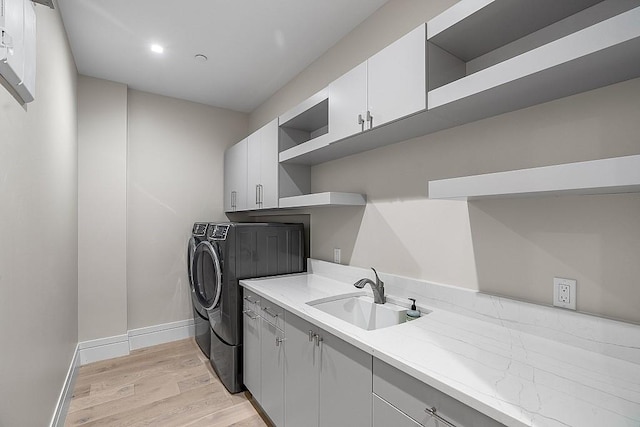 laundry area featuring cabinets, washing machine and dryer, sink, and light hardwood / wood-style flooring