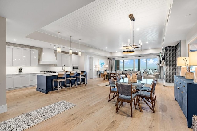 dining area with sink, an inviting chandelier, wooden ceiling, a raised ceiling, and light hardwood / wood-style floors