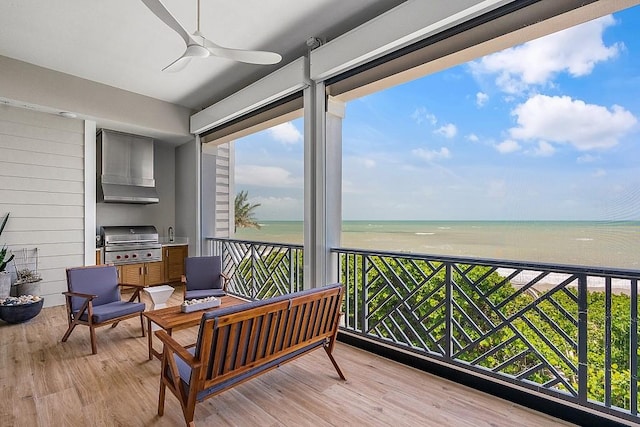 sunroom with a water view, ceiling fan, and a view of the beach