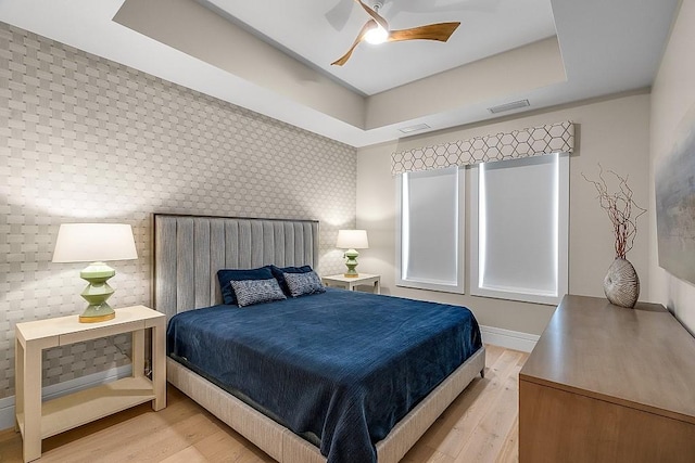 bedroom with a tray ceiling, ceiling fan, and light wood-type flooring