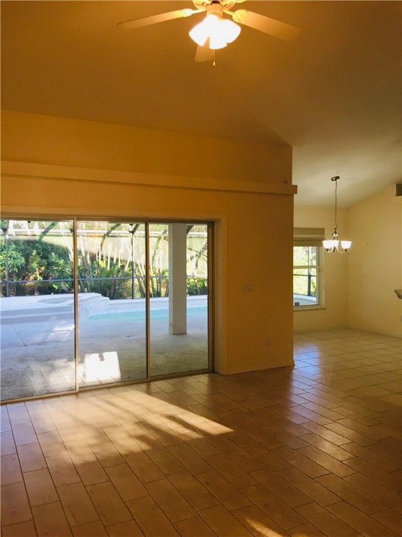 empty room with ceiling fan with notable chandelier, hardwood / wood-style flooring, and vaulted ceiling