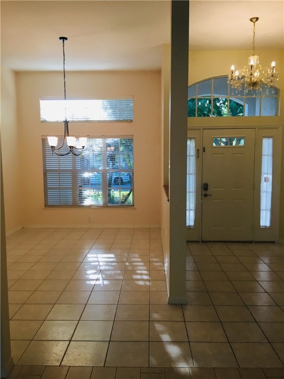 tiled entryway featuring a high ceiling, a healthy amount of sunlight, and an inviting chandelier