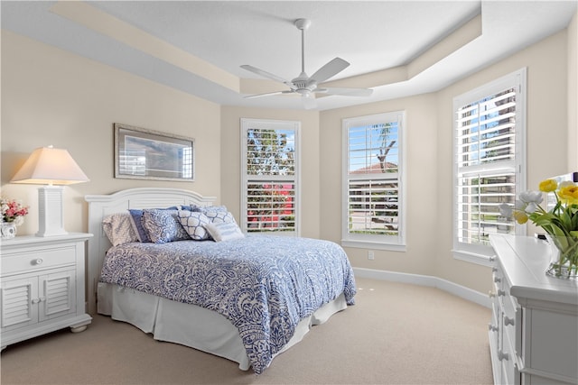 carpeted bedroom with ceiling fan and a tray ceiling