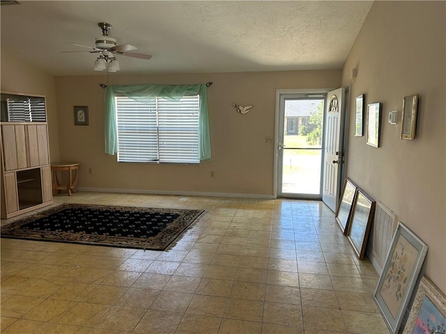 foyer entrance with ceiling fan, a textured ceiling, visible vents, and baseboards