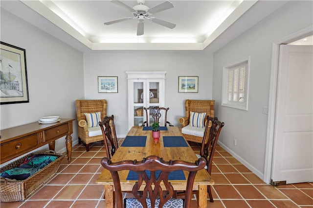 tiled dining room featuring ceiling fan, baseboards, and a raised ceiling