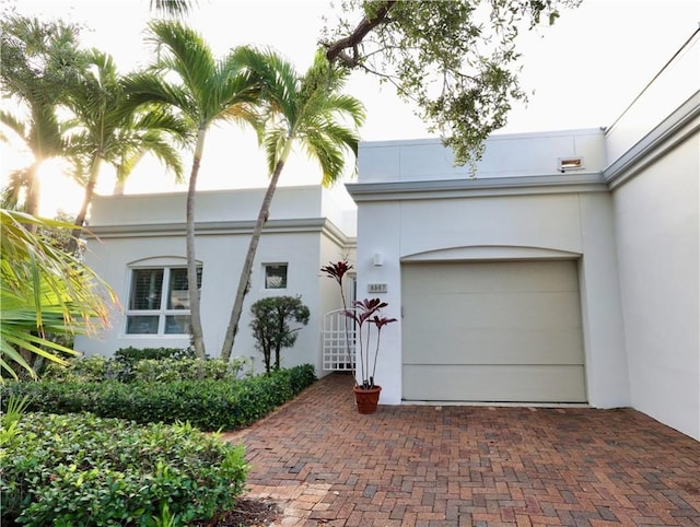 art deco inspired home featuring decorative driveway, an attached garage, and stucco siding