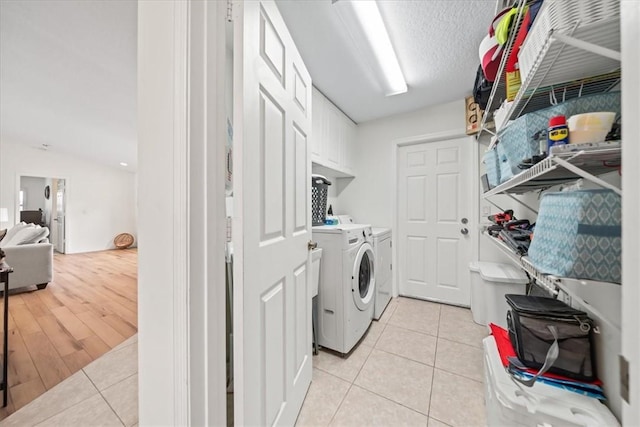 clothes washing area with washer and dryer, cabinets, a textured ceiling, and light tile patterned flooring