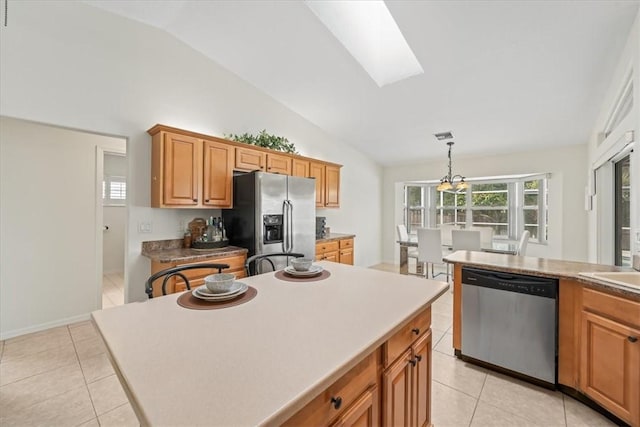 kitchen featuring vaulted ceiling with skylight, pendant lighting, appliances with stainless steel finishes, a center island, and light tile patterned flooring