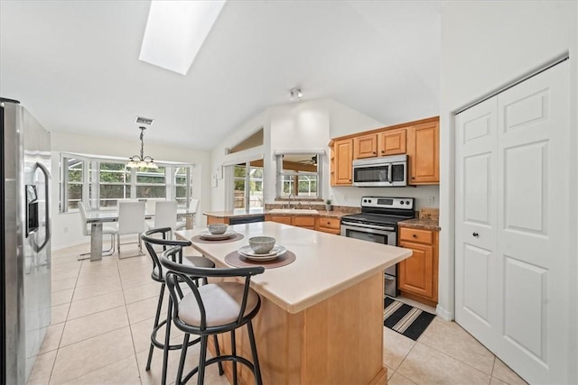 kitchen with light tile patterned floors, appliances with stainless steel finishes, lofted ceiling with skylight, pendant lighting, and a center island