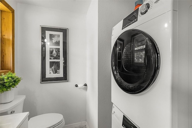 half bathroom featuring vanity, baseboards, toilet, and stacked washer and dryer
