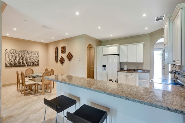 kitchen featuring kitchen peninsula, light stone countertops, stainless steel appliances, crown molding, and white cabinets