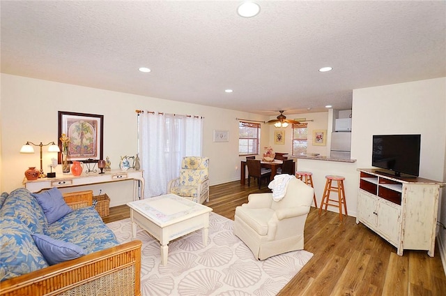 living room featuring light wood-type flooring, a textured ceiling, and ceiling fan