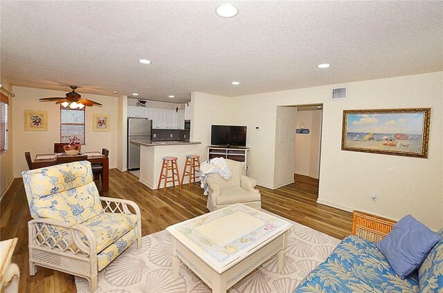 living room with ceiling fan, wood-type flooring, and a textured ceiling