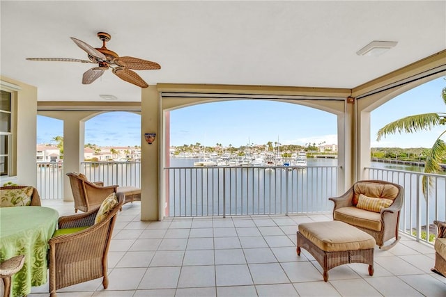 sunroom with ceiling fan and a water view